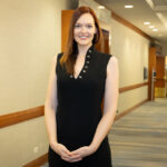 A woman in black dress standing next to wall.